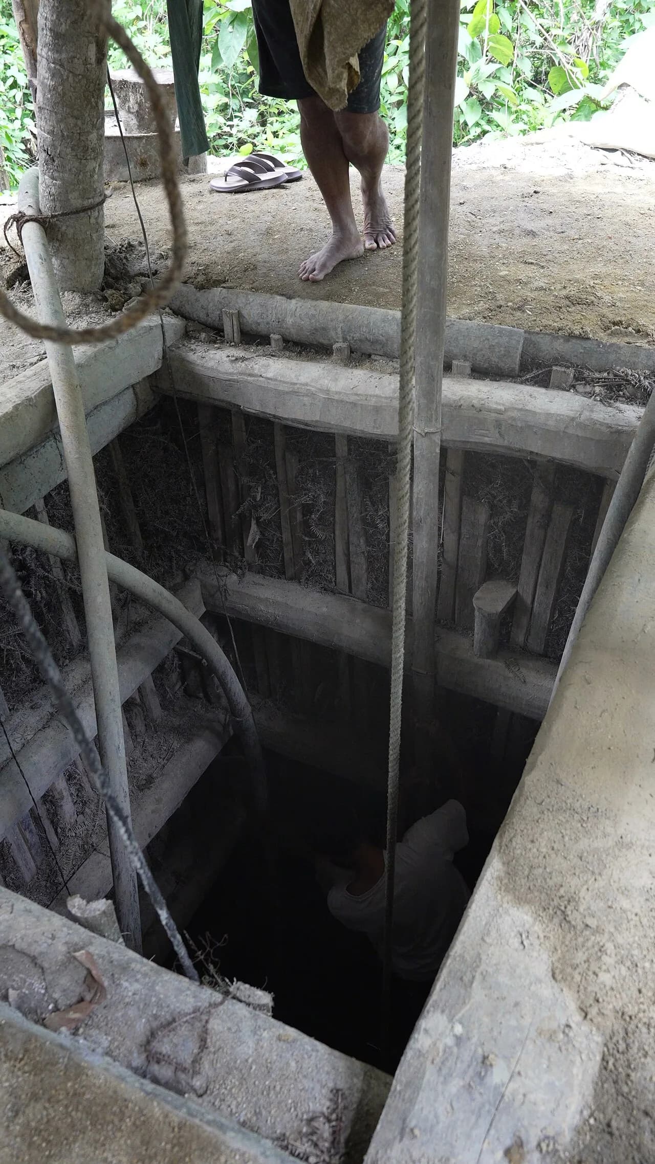 Ratnapura - Timber-lined shaft of an artisanal gem pit near Pelmadulla, Ratnapura District, Sri Lanka, seen from the pit head. A miner is visible at the bottom.